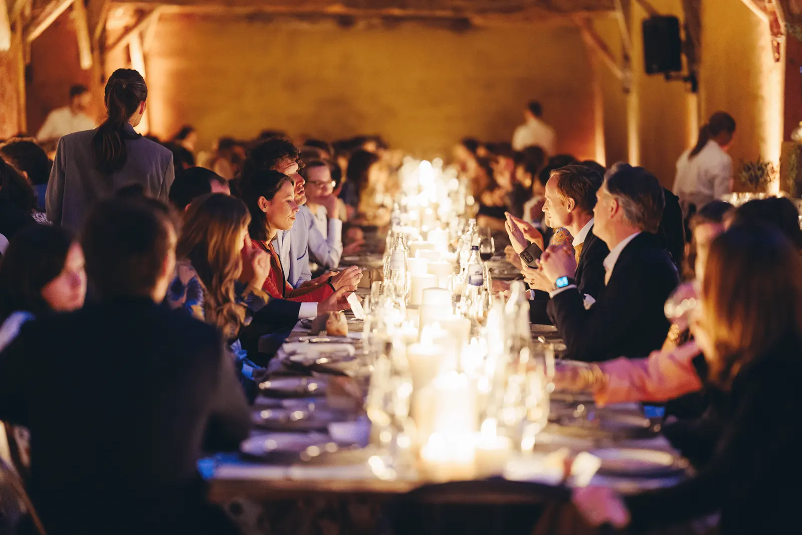 Gasten aan een lange tafel bij kaarslicht
